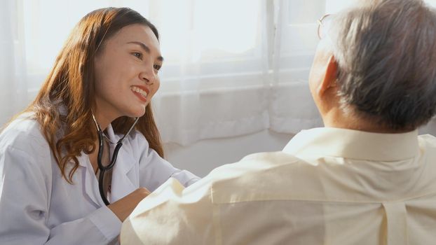 Female nurse doctor wear white uniform cardiologist examining patient senior or elderly old man during sit on wheelchair listening checking heartbeat using stethoscope at home, Health visitor concept