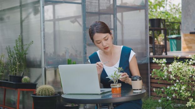 Asian beautiful lifestyle young woman talk selling small tree and cactus online by laptop computer social media live streaming, business online e-commerce distance near greenhouse, small business