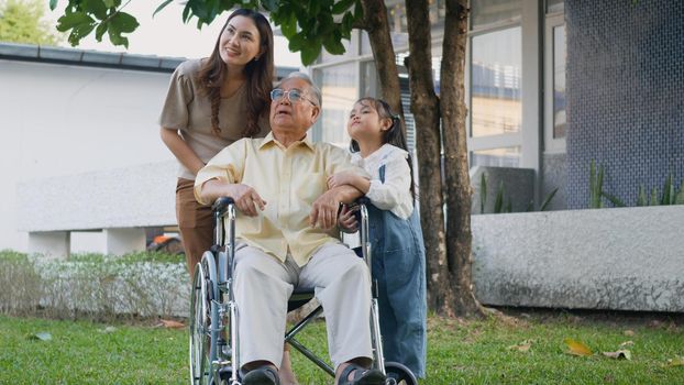 Disabled senior grandpa on wheelchair with grandchild and mother in park, Happy Asian three generation family having fun together outdoors backyard, Grandpa and little child smiling and laughed