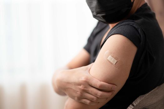 Man wearing mask arm with bandage showing his arm after receiving vaccine.