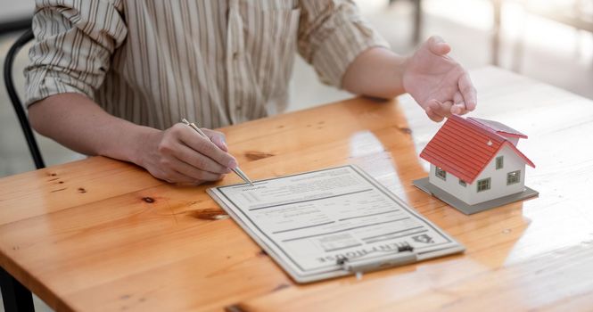 close-up view hands of businessman signing leasing home documents and have a house model on wooden desk.