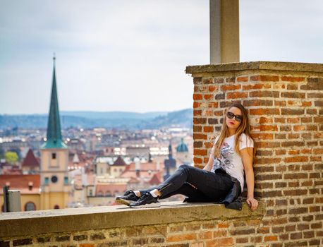A girl sits on a brick wall and admires the panorama of Prague. Travel