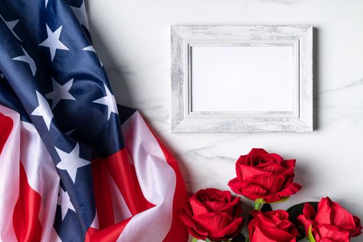 Concept of U.S. Independence day or Memorial day. National flag and red rose over bright marble table background with picture frame.