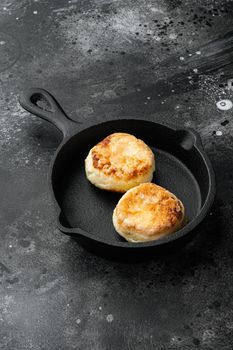 Pancake sweet curd fritters Syrniki set on cast iron frying pan skillet, on black dark stone table background, with copy space for text