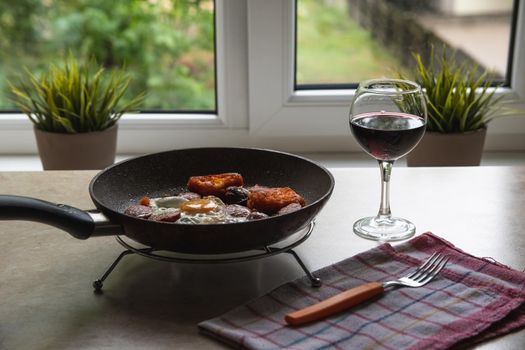 Barchelor breakfast - fried eggs with sausages on a teflon frying pan with glass of red wine