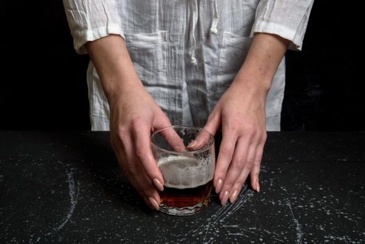 Woman hand holdin a glass with dark beer on black background