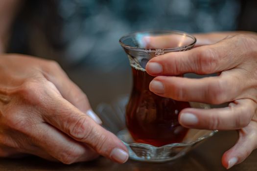 Hands of the elderly woman who holds a turkish glass with tea close up