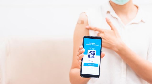 Asian young woman pointing to adhesive plaster on arm her vaccinated and showing app smartphone mobile digital screen vaccinated coronavirus (COVID-19) certificate after getting vaccine prevent