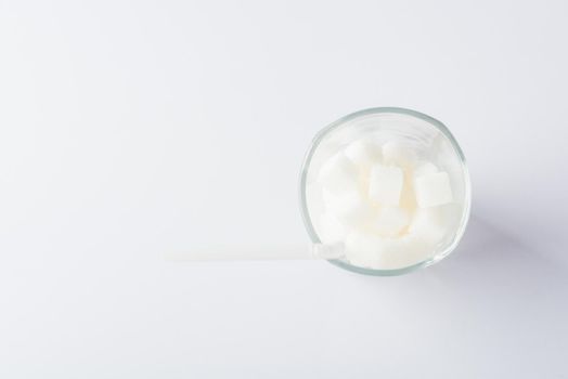 Top view glass full of white sugar cube sweet food ingredient, studio shot isolated on white background, health high blood risk of diabetes and calorie intake concept and unhealthy drink