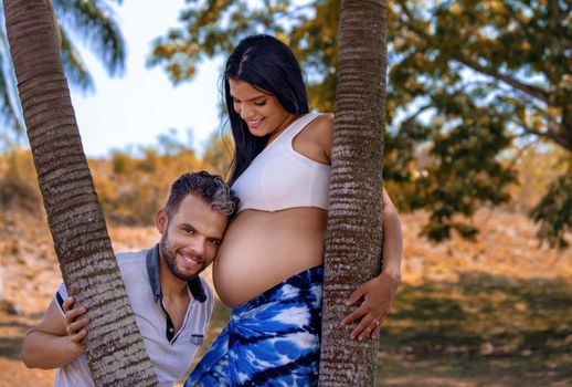 Photo of a young couple. The man's head is resting on the belly of the pregnant woman