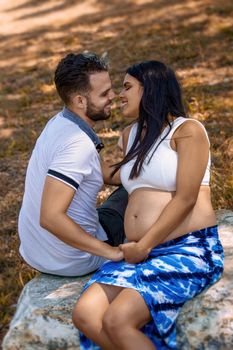 Photo of a young pregnant woman and a young man looking at each other sitting on a rock