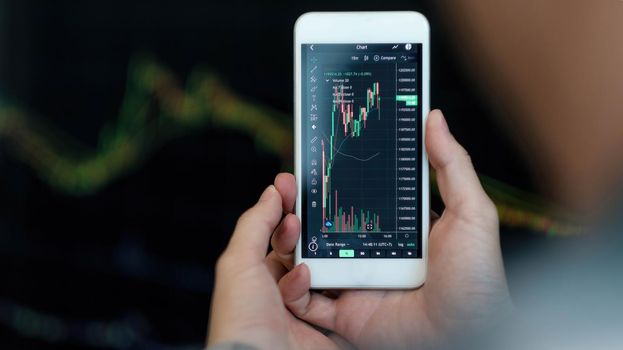 Business man trader investor analyst using mobile phone app analytics for cryptocurrency financial market analysis, trading data index chart graph on smartphone.
