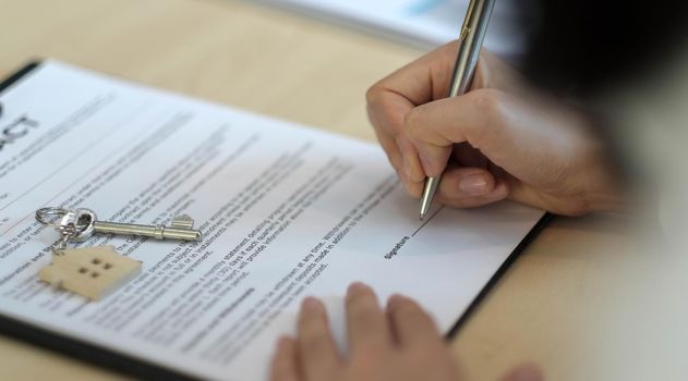 close-up view hands of businessman signing leasing home documents and have a apartment keys on paperwork..