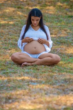 Young pregnant woman sitting on the grass looking at her tummy