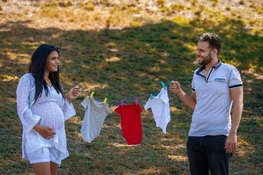 Young couple holding a twine with hanging baby clothes. The young woman is pregnant