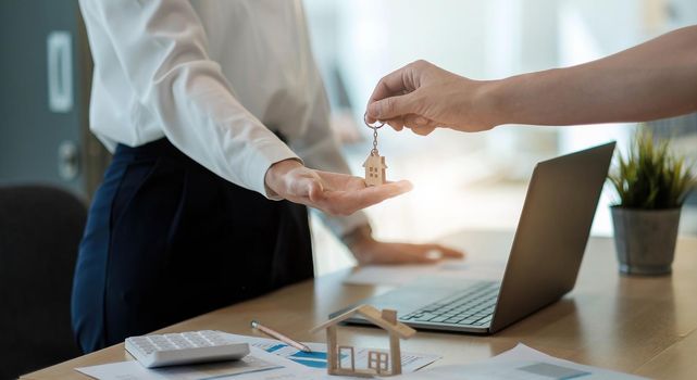 real estate agent holding house key to his client after signing contract agreement in office,concept for real estate, moving home or renting property.