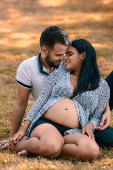 Young couple sitting on the grass. The young woman is pregnant