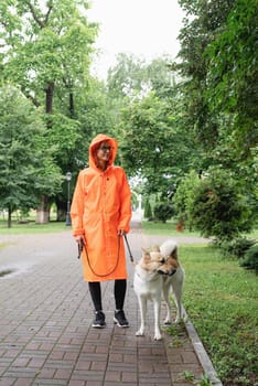 Rainy weather. Young woman in orange raincoat walking with her dog in a summer park