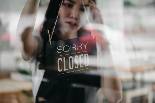 Close up shot of woman entrepreneur hand turning close sign board on glass door in coffee shop or restaurant during coronavirus lockdown quarantine.Owner small business, food and drink, business reopen again concept.