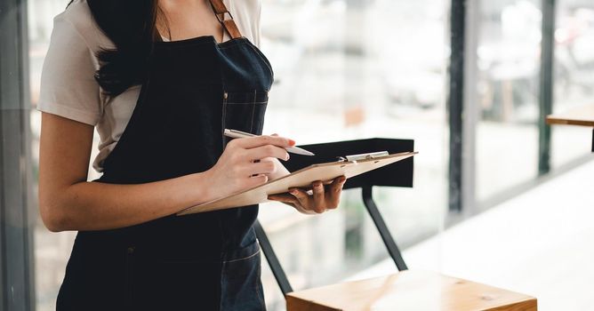 Close up female waitress take order cafe restaurant visitors couple, friendly professional woman server wear apron write dinner food menu choice, serving staff good customer service