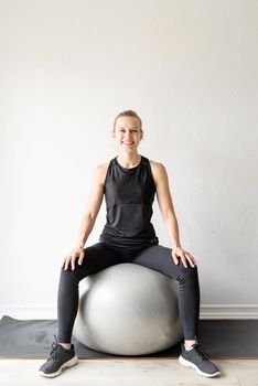 Sport and healthy lifestyle concept. Young sportive woman in black clothes sitting on the fitball warming out before workout