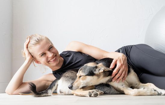 Sport and healthy lifestyle concept. Young sportive woman embracing her mixed breed dog laying on the floorat home