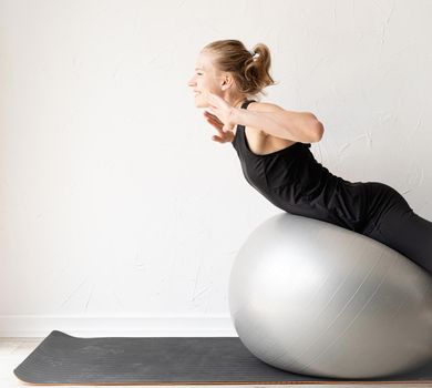 Sport and healthy lifestyle concept. Young smiling sportive woman working out on the fitness ball training her back