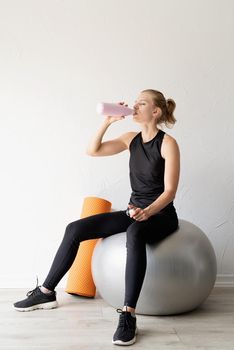 Sport and healthy lifestyle concept. Portrait of a young fit woman drinking water after working out with fitball