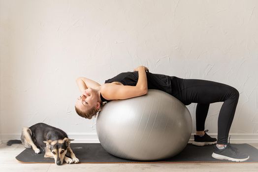 Sport and healthy lifestyle concept. Home fun. Young sportive woman in black clothes lying on the fitball warming out before workout