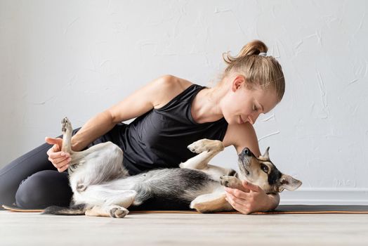 Sport and healthy lifestyle concept. Young sportive woman embracing her mixed breed dog laying on the floor at home