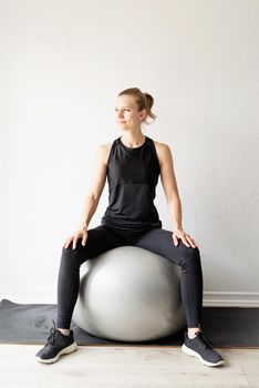 Sport and healthy lifestyle concept. Young sportive woman in black clothes sitting on the fitball warming out before workout