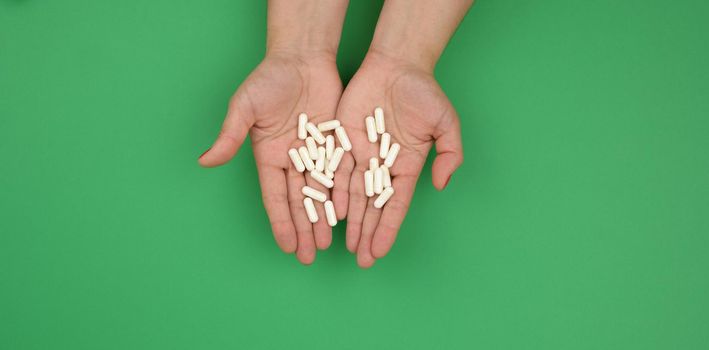 two female hands hold oval white capsules on a green background, top view