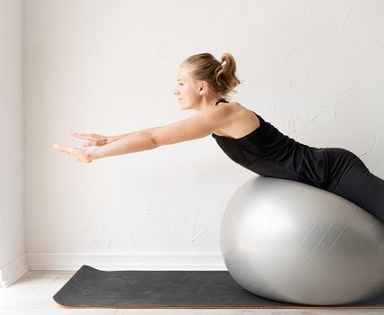 Sport and healthy lifestyle concept. Young smiling sportive woman working out on the fitness ball training her back