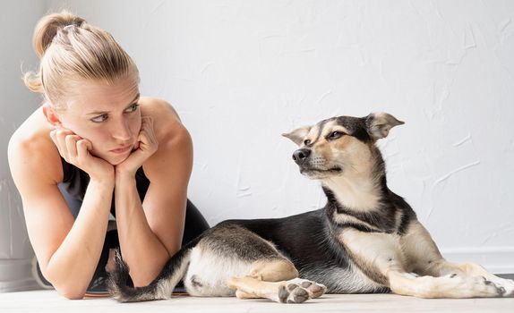 Young blond woman and her dog playing and having fun at home. Young sportive woman lying on the floor looking at her dog