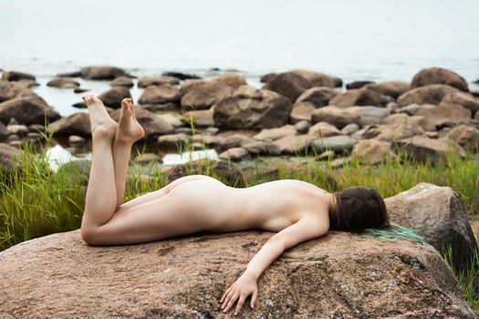 Lifestyle and beauty concept. Young nude woman enjoying nature among large stones by the sea. Naked woman on the seashore