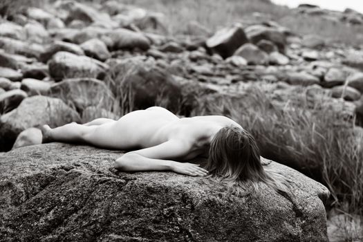 Lifestyle and beauty concept. Young nude woman enjoying nature among large stones by the sea. Naked woman on the seashore