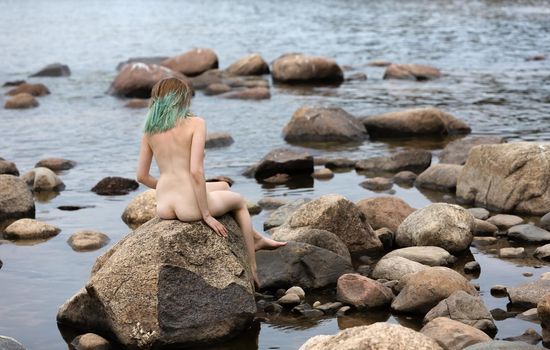 Lifestyle and beauty concept. Young nude woman enjoying nature among large stones by the sea. Naked woman on the seashore