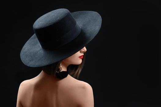 Rearview studio shot of a mysterious woman in a hat on black background red lips makeup cosmetics beauty fashion style elegance concept