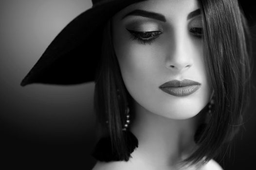 Monochrome close up of a gorgeous young stylish female fashion model posing sensually wearing professional makeup and a hat beauty cosmetics lips skin eyes hairstyle outfit retro vintage concept.