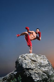 Young male boxer with strong ripped muscular body training outdoors kickboxing boxing fighting fighter abs courage stamina endurance energy activity athlete lifestyle sports sportive kicking concept.