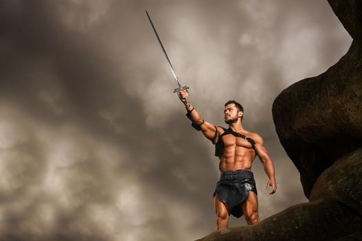 He will keep you safe. Low angle shot of a strong fierce warrior pointing his sword at the stormy sky standing on a rock copyspace