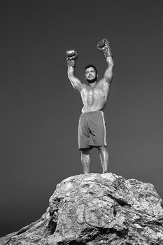 Monochrome low angle portrait of a boxing fighter wearing boxing gloves celebrating victory raising his arms in the air champion winner winning victorious goal achievement achieving pursuit.