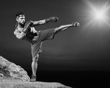 Black and white full length shot of a shirtless muscular man doing kickboxing training outdoors copyspace athletics physique fitness fit toned abs muscles strong powerful confident martial sportsman.