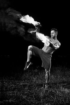 Monochrome shot of a shirtless muscular strong young male boxer practicing outdoors with his boxing gloves flaming with fire burning burn fiery force confidence martial combat fit muscles sweat agile.