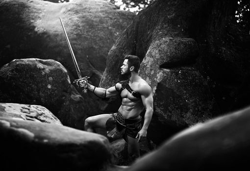 Strongest of men. Monochrome shot of a stunning powerful Spartan warrior lurking in the rocks with a sword copyspace