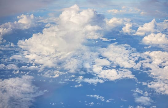 Fluffy sky clouds lit by afternoon sun, as seen from commercial airplane flying over.