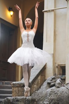 Graceful ballerina dancing near the building in the city posing elegantly with her arms raised in the air.