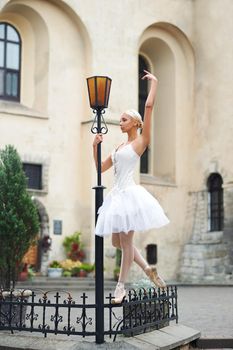 Graceful ballerina dancing outdoors on the city streets leaning on a street lamp gracefully.