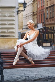 Vertical portrait of a graceful ballerina sitting alone on the bench in the city street grace elegance femininity sensuality loneliness art.