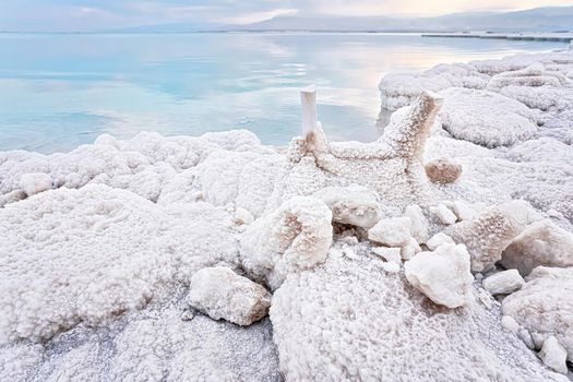 Small plastic chairs completely covered with crystalline salt on shore of dead sea, closeup detail, clear blue water near.